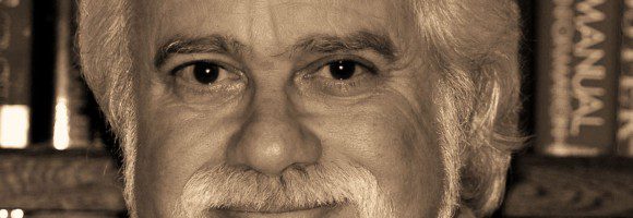 Portrait of an elderly man with white hair and beard in a cozy library.
